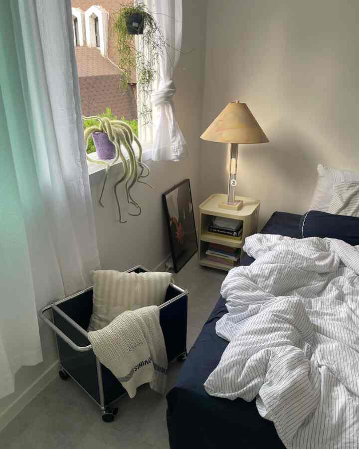 白とネイビーの色調の寝室、ナイトテーブルとフロアランプ、ストライプの寝具が配置された雰囲気のあるインテリア