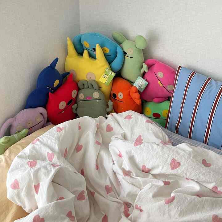 白とピンクのハート柄の寝具がある、カラフルなクッションとぬいぐるみで飾られたかわいい寝室