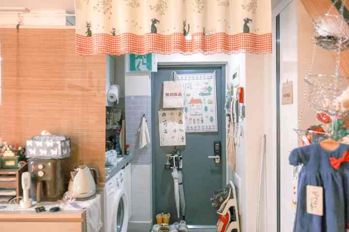 ホワイトとブルーの木目調が調和した狭い玄関兼キッチン兼ランドリールーム、バランスカーテンとファブリックポスターが配置された印象的な空間