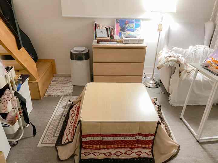 暖かいナチュラルトーンのリビングに中央のこたつとソファ、毛布が配置された居心地のよいインテリア