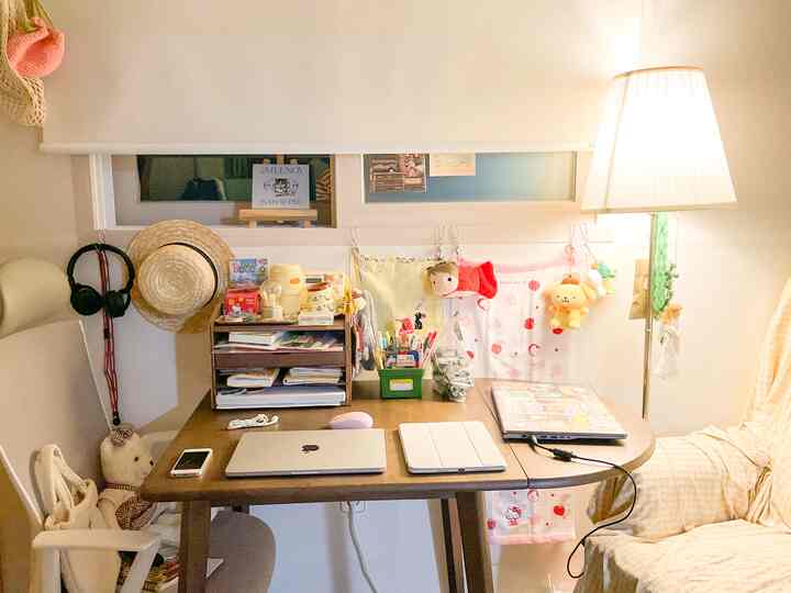 ナチュラルな色調のコンパクトな部屋、中央に木製のデスクとオフィスチェア、右側にソファとフロアランプが配置された落ち着いたホームオフィスのインテリア