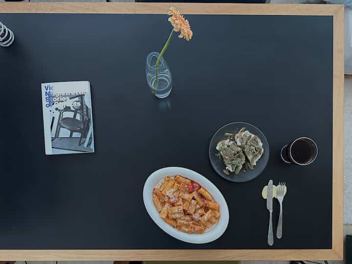 黒い天板と明るい木製の縁取りがあるダイニングテーブルに料理とアイスコーヒーが置かれた落ち着いた空間