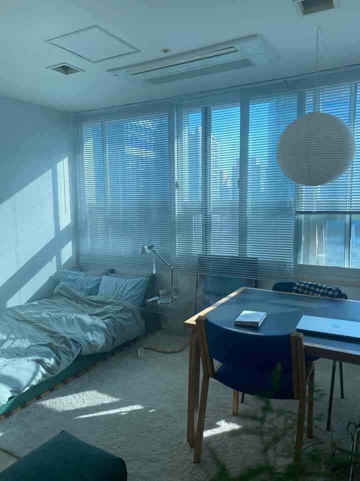 白と青の色調の寝室空間、壁際に配置されたベッドと窓辺のブラインドがある落ち着いた雰囲気のインテリア