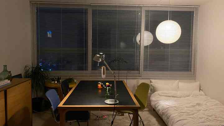 ホワイトの壁とブラインドがあるミッドセンチュリーモダンスタイルの寝室兼おうちカフェ空間、中央にブラックのデスクと色鮮やかな椅子を配置した雰囲気のあるインテリア