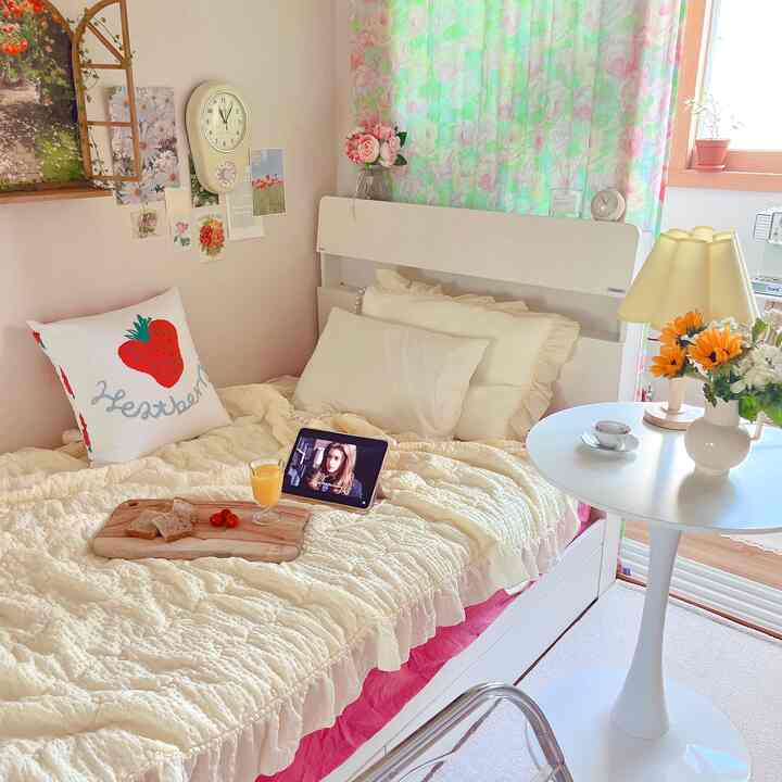 パステルの花柄カーテンとアイボリーの寝具、花瓶とテーブルランプが配置された印象的な一人暮らしの寝室