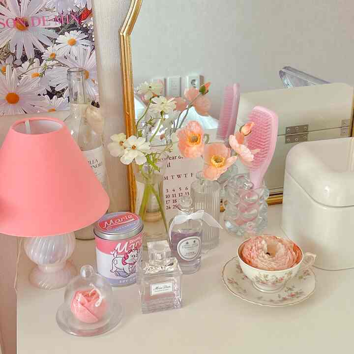 ピンクと白のトーンが調和した化粧台の空間、ヴィンテージ小物や花瓶、香水が美しく配置された雰囲気のあるインテリア