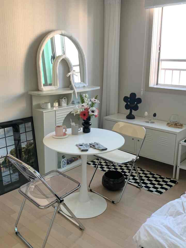 白を基調にした小さな部屋、丸テーブルと折りたたみ椅子2脚、収納キャビネットが配置されたミニマルな空間