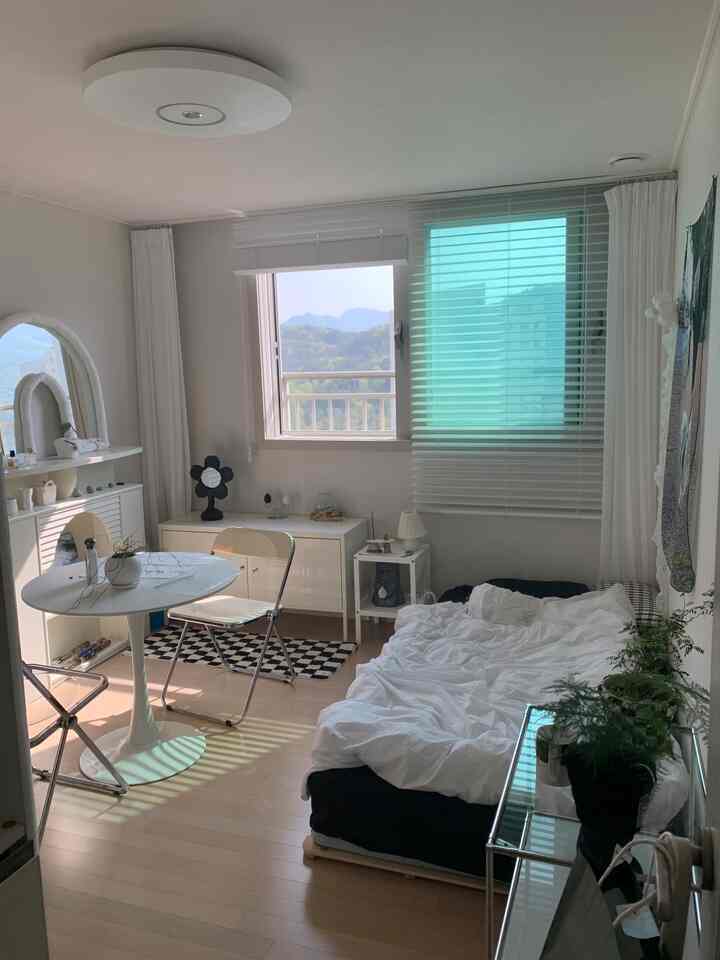 明るいホワイトとウッドトーンの調和したコンパクトな寝室、シンプルなベッドとテーブルが配置されたナチュラルモダンなインテリア