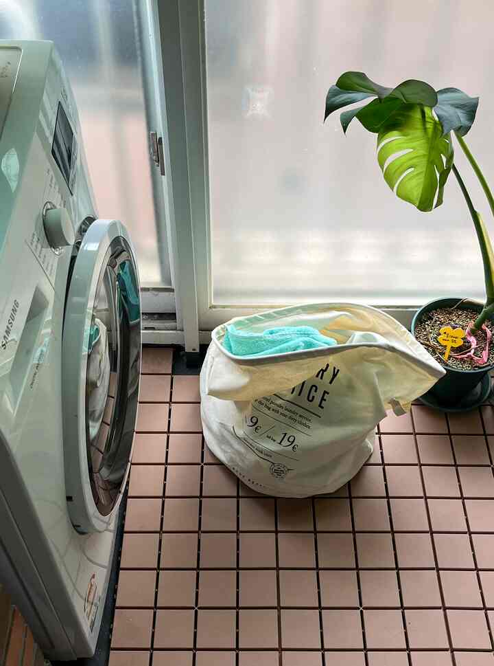 淡いブラウンの床タイルが敷かれたバスルーム、洗濯機と布製のランドリーバスケットが配置された清潔感のある空間