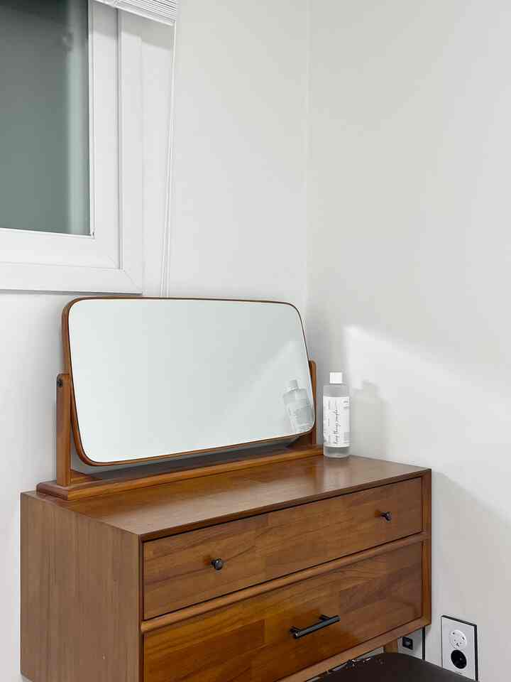 白い壁とブラウンの木製化粧台が配置されたシンプルですっきりとした寝室の一角