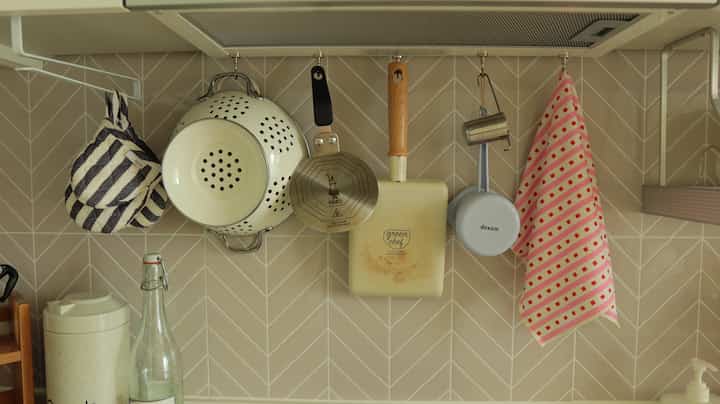 ベージュ色調のキッチンの壁、フライパンやざる、キッチンタオルが掛けられた雰囲気のあるインテリア