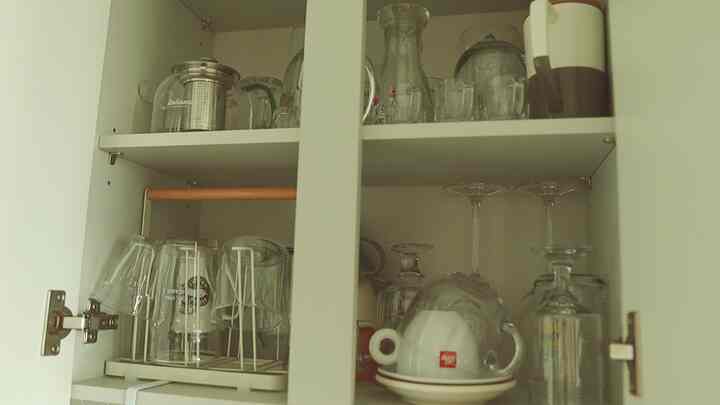 ホワイトカラーのキッチン収納棚に透明な食器やワイングラスがきれいに整理されたミニマルな雰囲気の空間