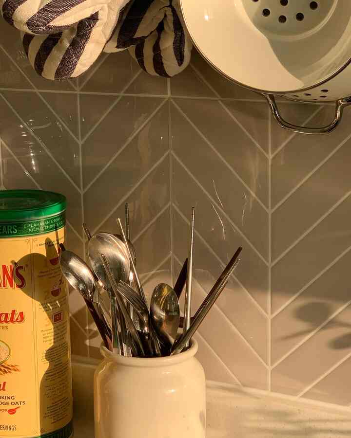 暖かいアイボリーとブラウンの色調のキッチン、中央にステンレス製のスプーンと箸が入ったアイボリーのカトラリースタンドが配置された印象的な空間