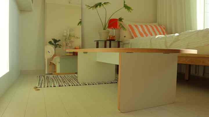 明るいナチュラルカラーのリビング、座卓とベッド、カーテンが配置された落ち着いた空間