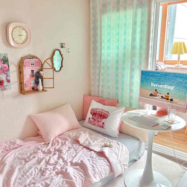 ピンクと青のトーンの寝室、壁掛け収納とコンピューターモニターが配置された印象的で明るいインテリア