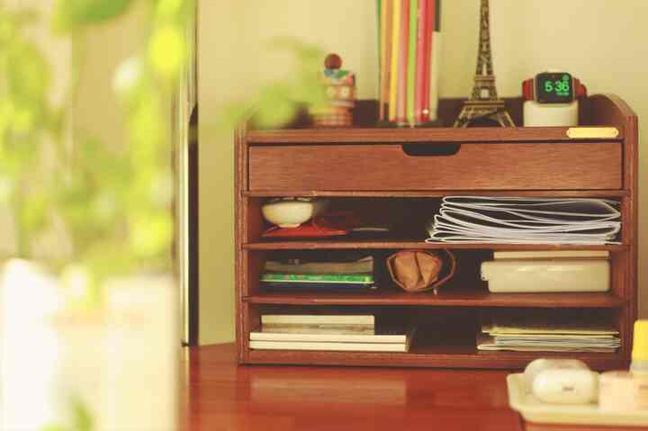 温かみのある木目調のデスクの上にコンパクトな書類収納棚と装飾品が配置された居心地の良いホームオフィス空間