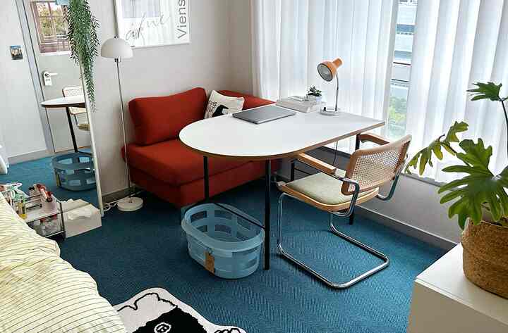 ネイビーの大きなラグと赤い一人用ソファ、白いデスクとアームチェアが配置された明るく居心地の良いホームオフィス空間