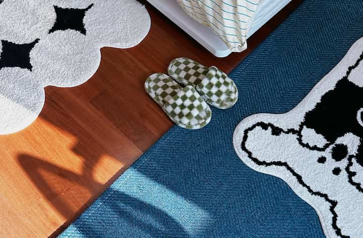 白と青のトーンのワンルーム床、パターンラグとチェック柄のスリッパが配置された温かみのある空間