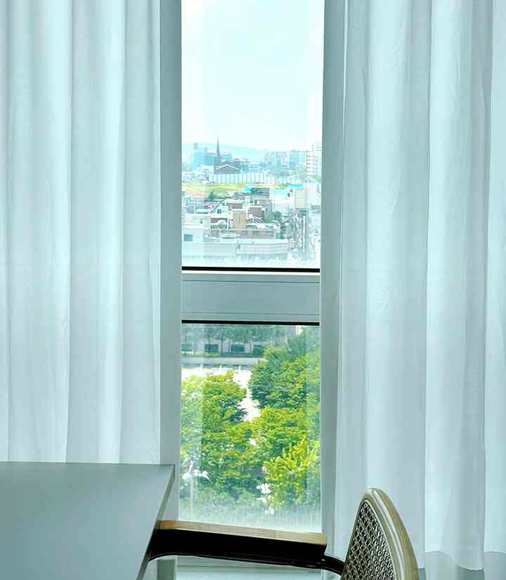 明るい白色のダイニングルームの窓と白いカーテン、都市の景色と緑が見えるバルコニーのある雰囲気のあるインテリア