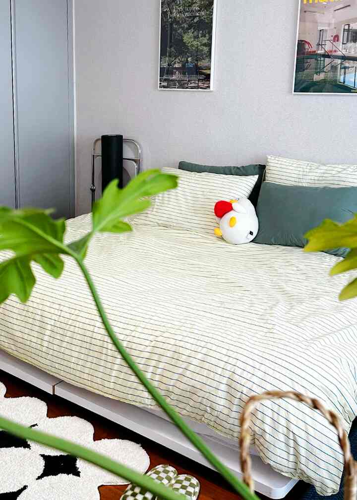 ベージュとグリーンのトーンの寝室、中央にロータイプベッドフレームとクッションが配置された雰囲気のある空間