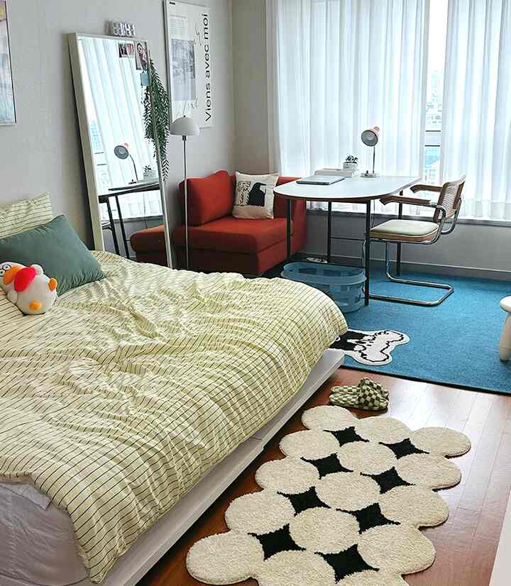 黄色の寝具と赤いソファが配置された一人暮らしの寝室、窓際に机と鏡がある雰囲気のある空間