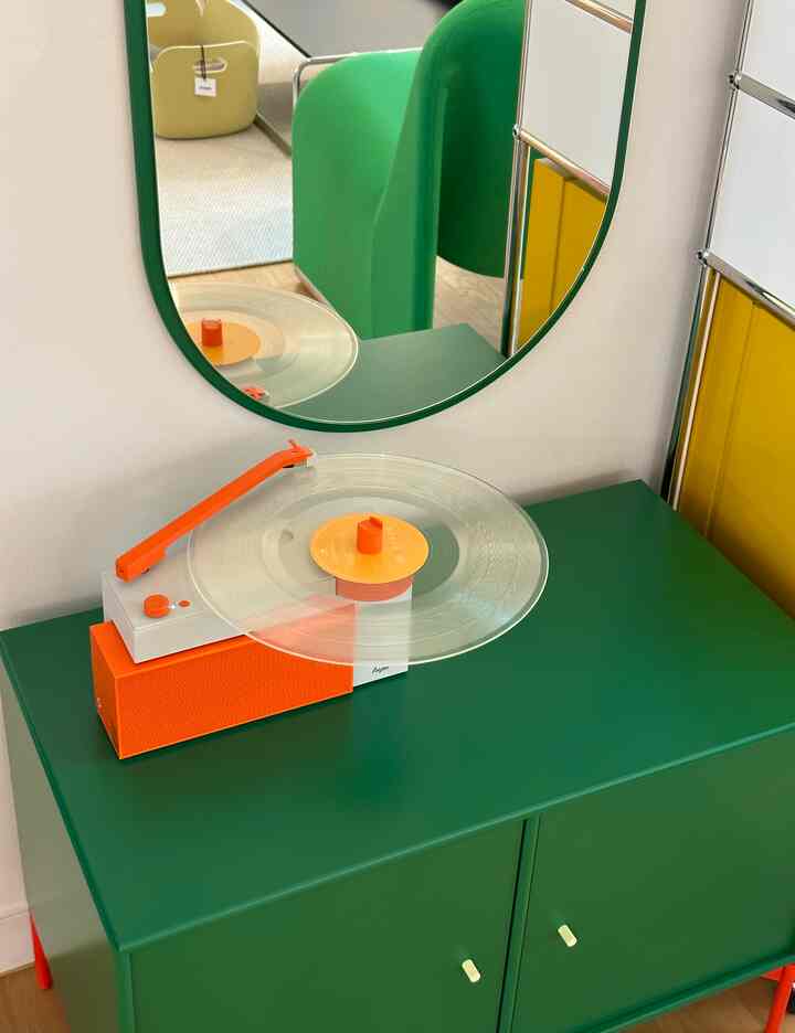 深い緑のキャビネットとオレンジのアクセントがあるターンテーブルが緑色の鏡の下に配置された、レトロな雰囲気のキッチンスペース