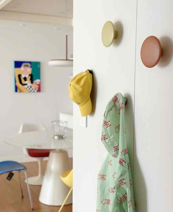 白い壁と木目調の床が調和するモダンダイニングルーム、壁にはMuutoのThe Dotsコートフックが設置され、ジャケットと帽子が整頓された空間