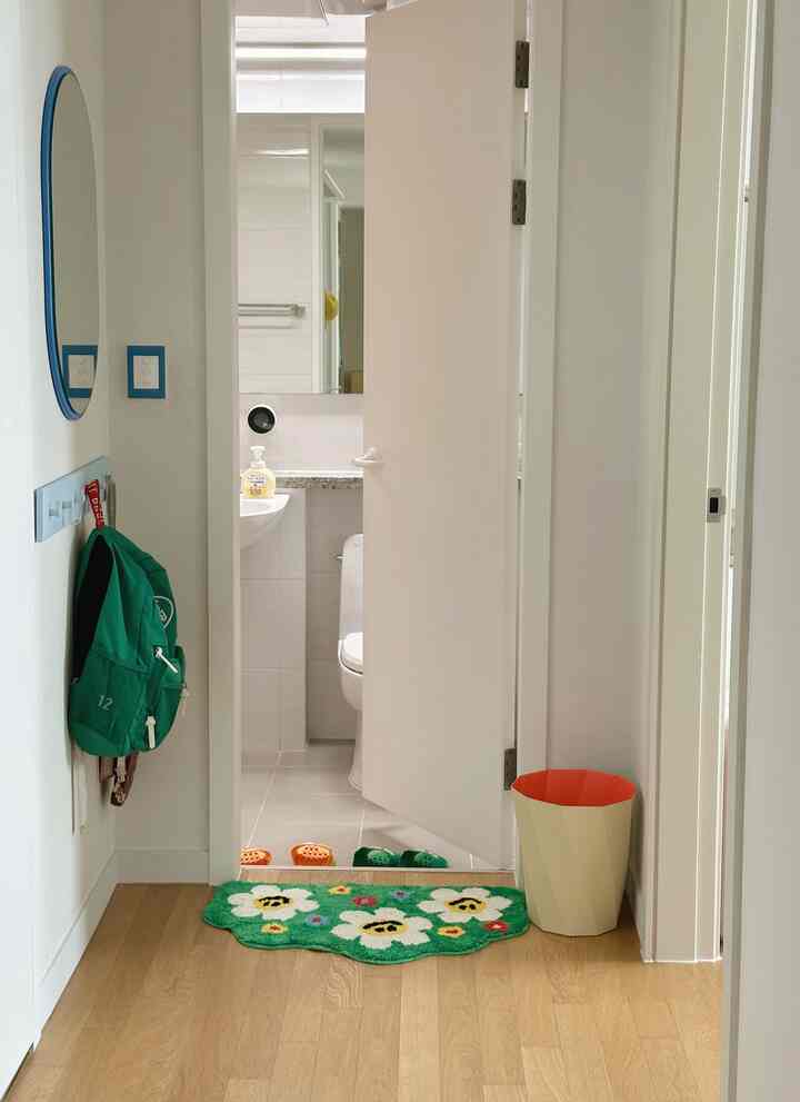 白と木目調の床が調和した廊下、ネイビーフレームの丸い鏡と子供のバッグが掛かったコートハンガーが配置された清潔感のある空間