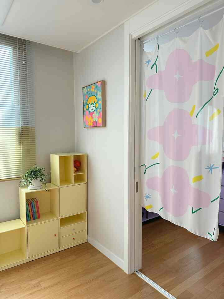 白い壁と木目調の床が印象的な子供部屋のコーナー、黄色い棚と鮮やかな柄のカーテンで雰囲気のあるインテリア