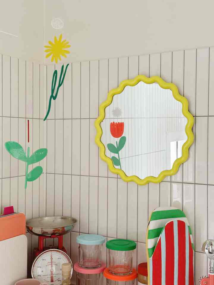 ベージュのタイル壁に黄色い波形の鏡と黄色い花のモビールがあるシンプルなキッチン空間