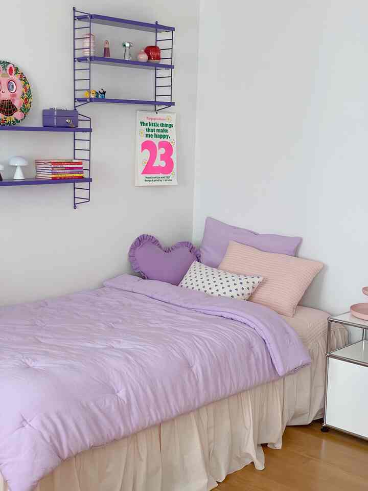 ラベンダー色調の寝室、柔らかいベッドと枕、ナイトテーブル、壁に設置された棚が配置された雰囲気のあるインテリア