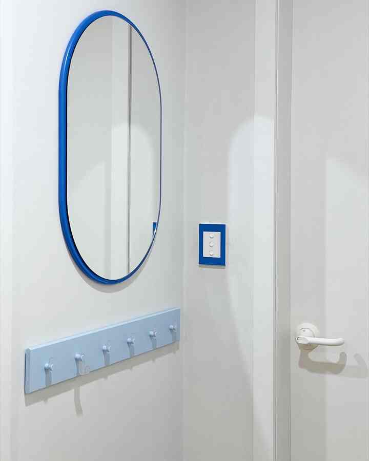 白い壁と扉の玄関、ブルーフレームの鏡とスイッチが調和した清潔感のある空間