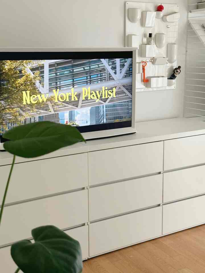 白と木目調床が調和したミニマルなリビング、テレビ台と壁掛け収納が配置された清潔感のある空間