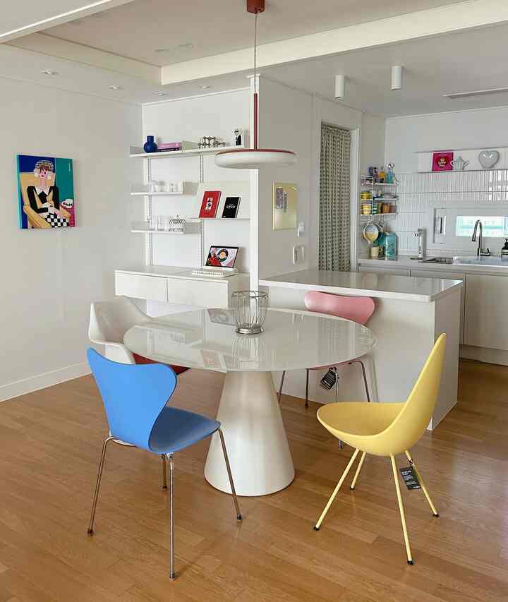 白と木目調の調和が美しいダイニング、カラフルな椅子とモダンな丸テーブルが配置されたシンプルな空間