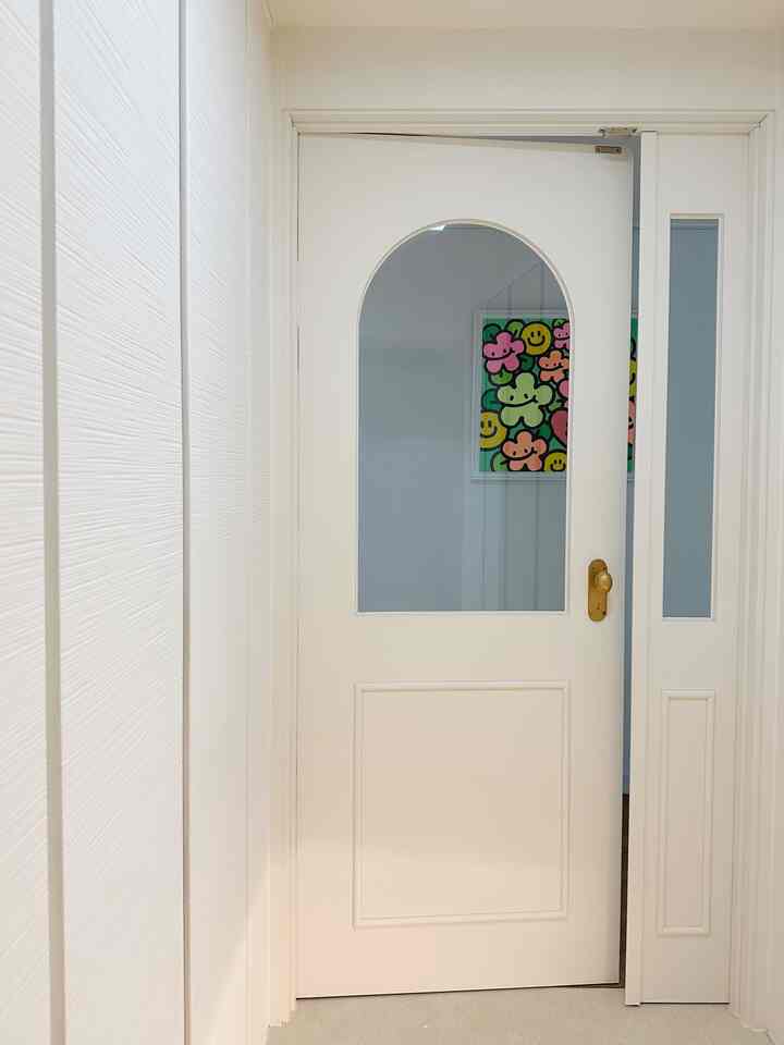 白を基調とした玄関、アーチ型のドアとキム・バル氏のカラフルな額縁アートが配置されたシンプルな空間