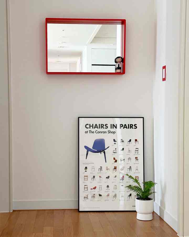 白い壁と木目調の床、赤い額縁の鏡とポスターが配置されたミニマルな玄関のインテリア