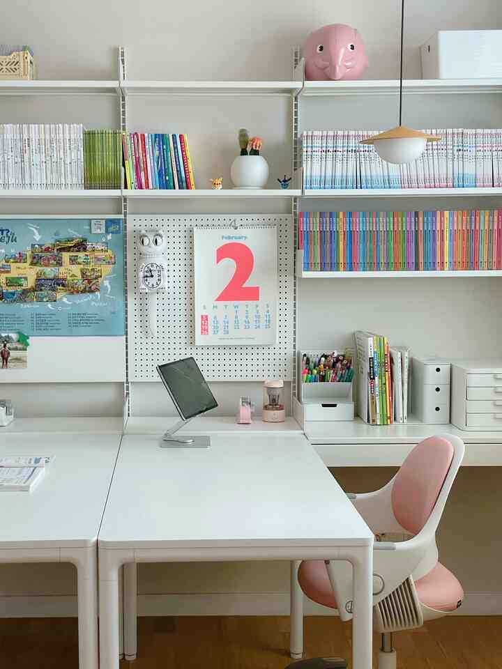 白を基調としたホームオフィス、広いデスクと本棚、ピンクのオフィスチェアが配置された清潔感のある実用的なインテリア