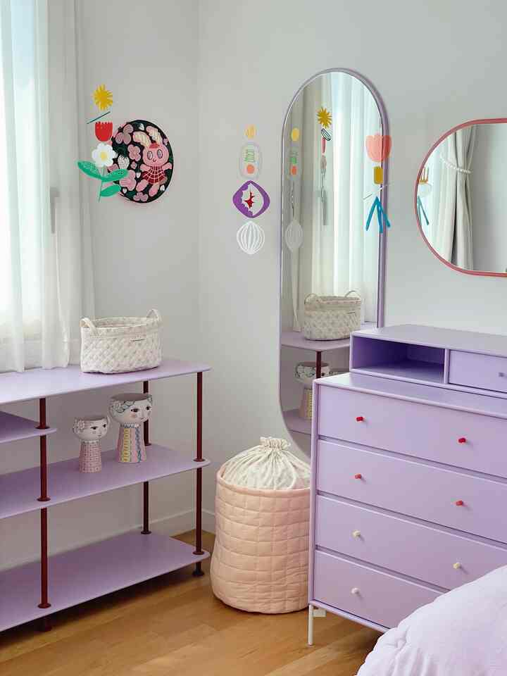 白い壁とラベンダーカラーのドレッサーと棚が配置された、温かみのある小さな居心地の良い部屋