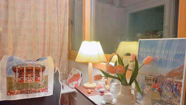 ピンクとナチュラルカラーのトーンのベランダのデスクスペース、花瓶と照明、ポスターが配置された雰囲気のあるインテリア