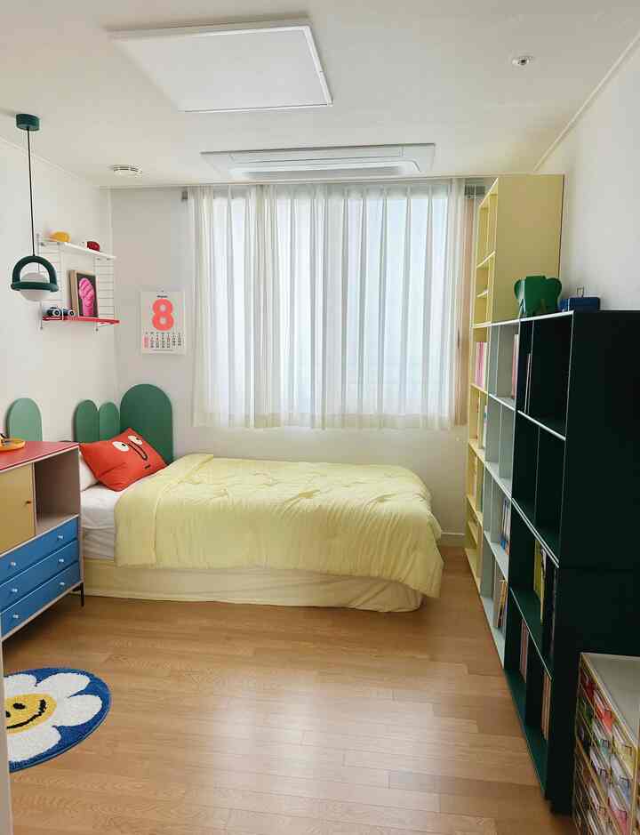 ホワイトとウッドトーンの子供部屋、黄色いベッドカバーと本棚が配置された雰囲気のある空間