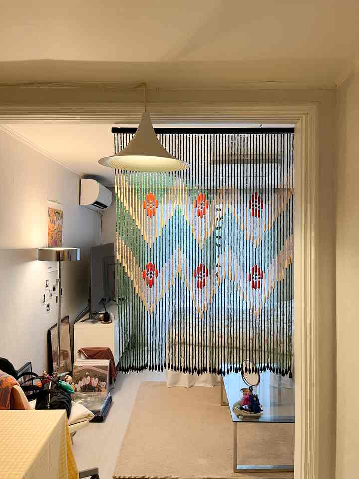 ナチュラルな色調の玄関から見たリビング、木製ビーズカーテンとベージュのラグが配置された印象的な空間