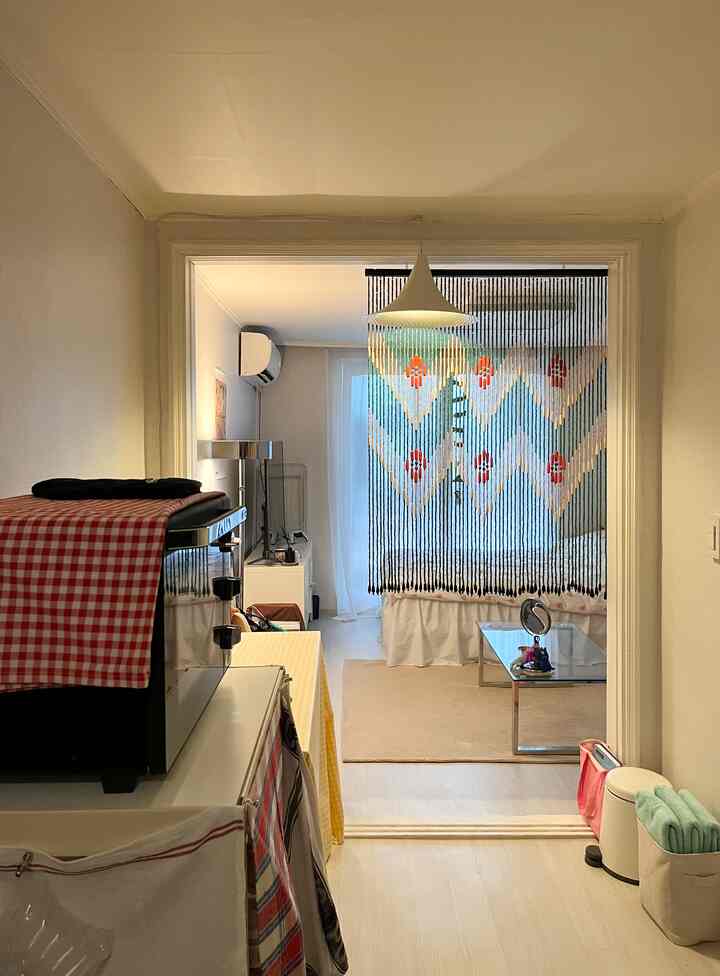 白とベージュのトーンでまとめられたワンルームのキッチン兼リビング、チェック柄のテーブルクロスが置かれたシンプルな調理台と清潔な空間