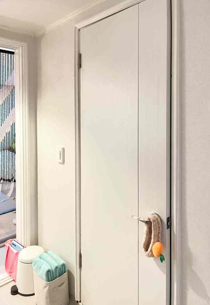 白を基調としたトイレの入口、ドア横にミント色のタオルとゴミ箱が配置された清潔感のある空間