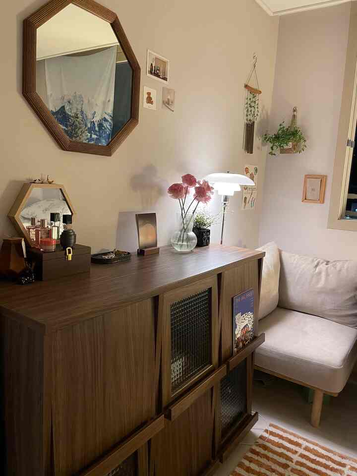 ベージュの壁とナチュラルな木目調の収納がある居心地の良いリビング、花とスタンドライトが配された自然な雰囲気のインテリア