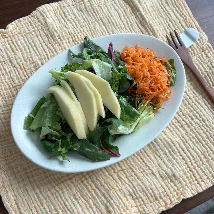 ナチュラルカラーのキッチン小物で、クリーム色のマットな皿に新鮮なサラダとにんじんが盛られ、木製フォークと黄色いテーブルランナーが配置された雰囲気のあるおうちカフェインテリア