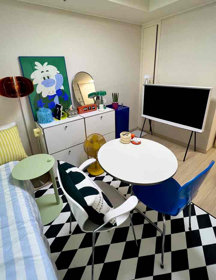 ホワイトとビビッドカラーが調和する7坪のワンルーム、丸型ダイニングテーブルとセリフTVが配置されたモダンな寝室兼リビングスペース