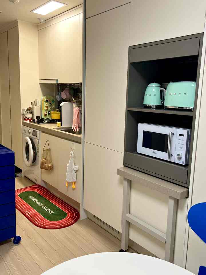 ナチュラルな色調のワンルームキッチン、モダンなクローゼットと電子レンジ、小型家電が整然と配置された雰囲気のあるインテリア