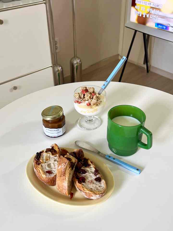 白いテーブルにパン、ヨーグルトボウル、ジャム、グリーンのマグカップが配置された雰囲気のあるカフェ風キッチン