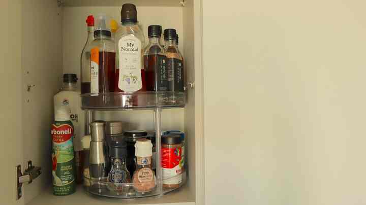 明るいベージュ色調のキッチンキャビネット内に透明な2段回転トレイがあり、様々な調味料瓶が整理された実用的な収納スペース