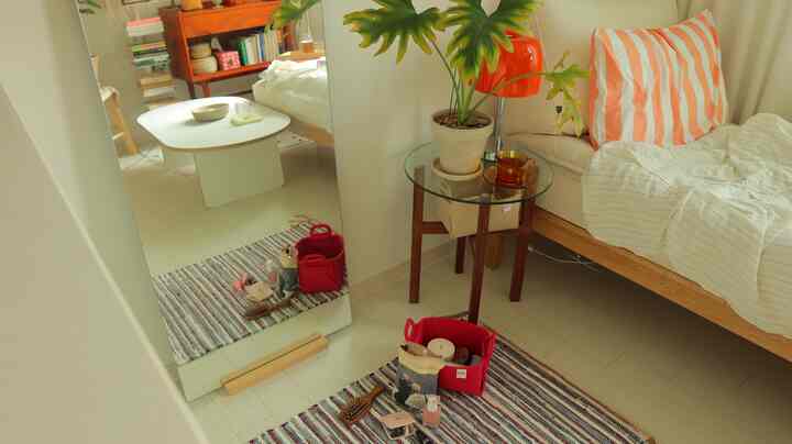 ナチュラルなトーンの狭い寝室、木製ベッドと丸いナイトテーブル、大きな全身鏡、化粧品バスケットを置いた化粧台スペース